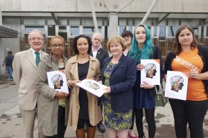 A group of people holding copies of the mental health consultation look into the camera. One lady, the minsiter for mental health, accepts a copy of the consultation from one of the others present.
