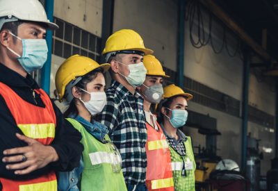 The image shows a line of workers wearing medical masks to protect themselves from coronavirus.