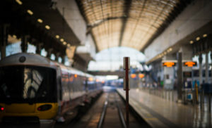 Photo showing a railway train station, with a train on the left and the platform on the right.