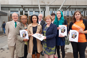A group of people holding copies of the mental health consultation look into the camera. One lady, the minsiter for mental health, accepts a copy of the consultation from one of the others present.