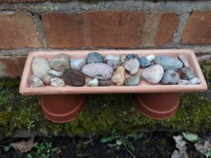 A shallow dish filled with clean stones is placed on top of two upturned plant pots