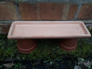 A shallow dish is placed on top of two upturned plant pots