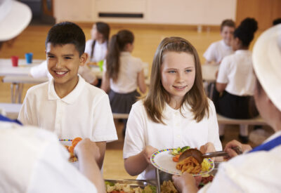 Two children in school uniform are given their school lunch