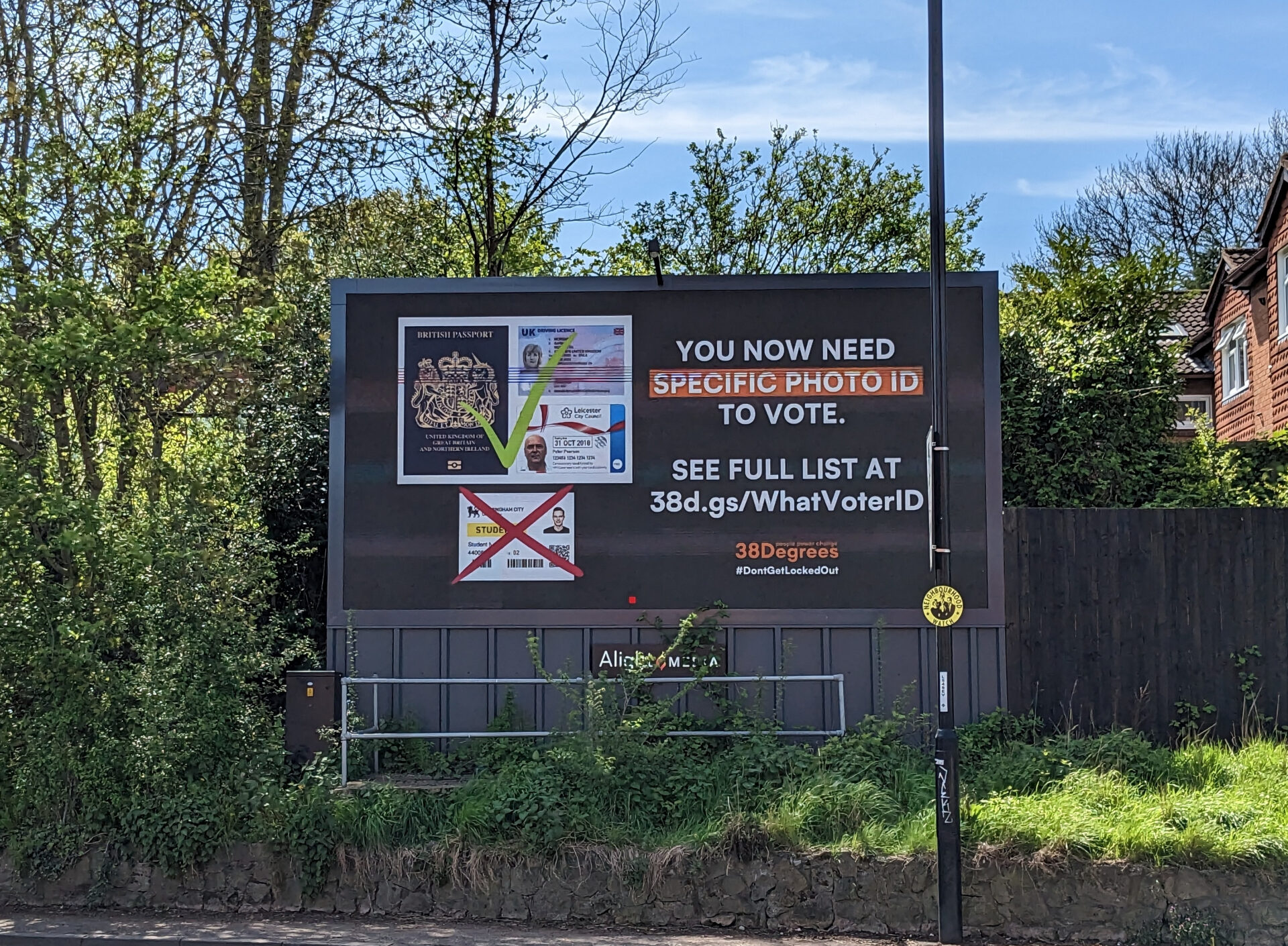 A large billboard against a leafy green background and blue sky warns people "you now need specific ID to vote"