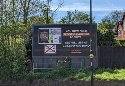 A large billboard against a leafy green background and blue sky warns people "you now need specific ID to vote"