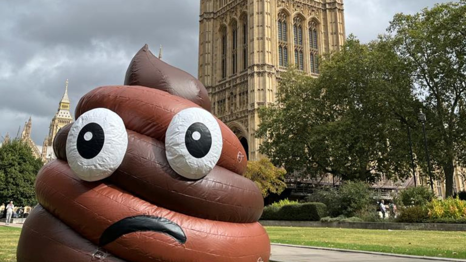 A giant inflatable poo emoji in the green by Houses of Partliament.